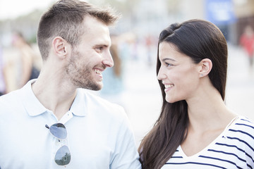 Funny couple laughing with a white perfect smile and looking each other outdoors with unfocused background. Love concept