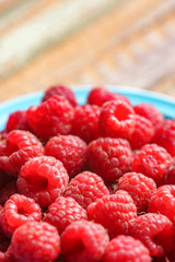 Red rasberry in blue green dish on old vintage wooden table.