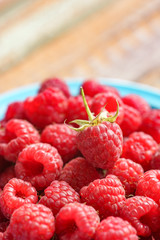 Red rasberry in blue green dish on old vintage wooden table.