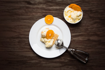 Orange ice cream with waffle and fruits on the dark wooden background