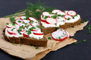 Two sandwiches with sour cream, onions and radishes and dill on a package on a isolated  black background