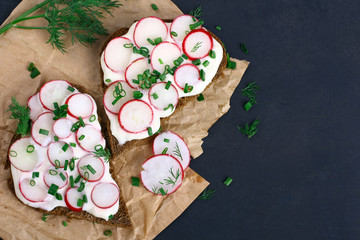 Two sandwiches with sour cream, onions and radishes and dill on a package on a isolated  black background