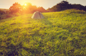 Tourist tent on green meadow at sunrise. Camping background.