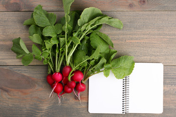 Red radishes nearby to the open notebook on a  brown wooden table
