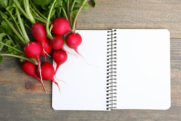 Red radishes nearby to the open notebook on a  brown wooden table