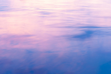 Abstract background light on water as colors of clouds at sunset reflect with pink transitioning to blue in the surface ripples.