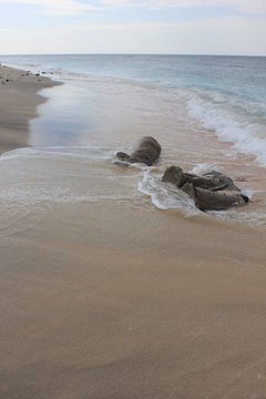 Tropical Indonesian Gili Islands beach water's edge in a dull day with a rocj in the middle