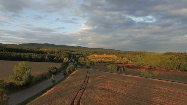 Aerial fly over golden fields and green forests of Central European countryside on a clear lovely summer sunset