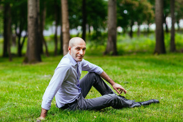 Portrait of a bald and brutal man. Bald guy sitting on the grass