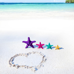 Fototapeta na wymiar Heart on beach with color starfishes
