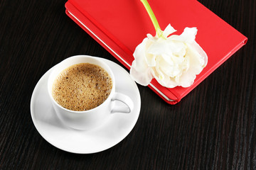 Cup of coffee with notebook and fresh flower on wooden table background