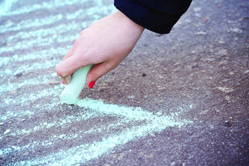 Female hand drawing arrow by chalk on pavement