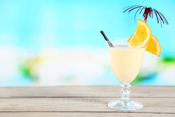 Glass of summer cocktail on wooden table on bright blurred background