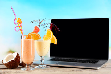 Laptop and glasses of summer cocktails on wooden table, on bright blurred background
