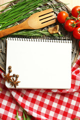 Open recipe book with fresh herbs, tomatoes and spices on wooden background
