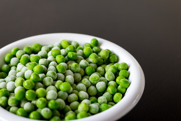 A white bowl with frozen green peas in the kitchen