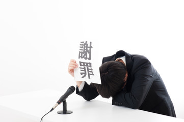 記者会見でマイクを使って謝罪している役員