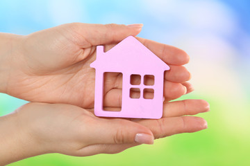 Female hands holding model of house on bright background