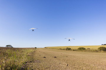 Flying microlight aircraft planes take-off on rural grass airstrip.