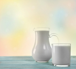 Pitcher and glass of milk on wooden table, on bright background