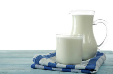 Pitcher and glass of milk on wooden table, on white background