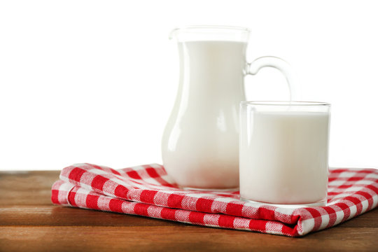 Pitcher and glass of milk on wooden table, on white background