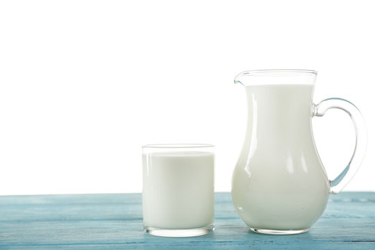 Pitcher and glass of milk on wooden table, on white background