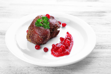 Tasty roasted meat with cranberry sauce on plate, on color wooden background