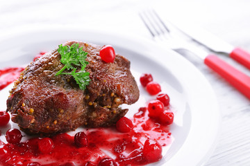 Tasty roasted meat with cranberry sauce on plate, on color wooden background