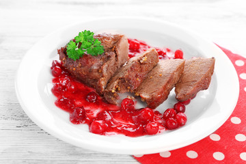 Tasty roasted meat with cranberry sauce on plate, on color wooden background