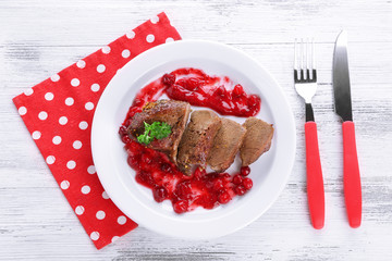 Tasty roasted meat with cranberry sauce on plate, on color wooden background