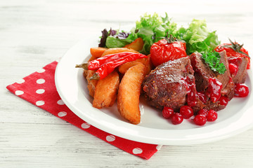 Tasty roasted meat with cranberry sauce and roasted vegetables on plate, on color wooden background
