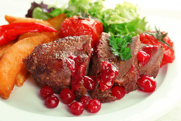Tasty roasted meat with cranberry sauce and roasted vegetables on plate, on color wooden background