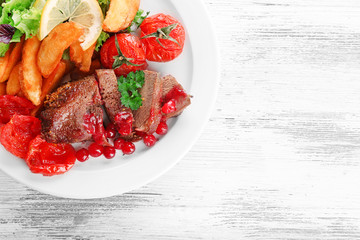 Tasty roasted meat with cranberry sauce and roasted vegetables on plate, on color wooden background