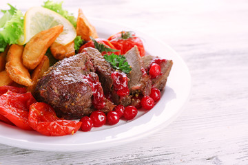 Tasty roasted meat with cranberry sauce and roasted vegetables on plate, on color wooden background