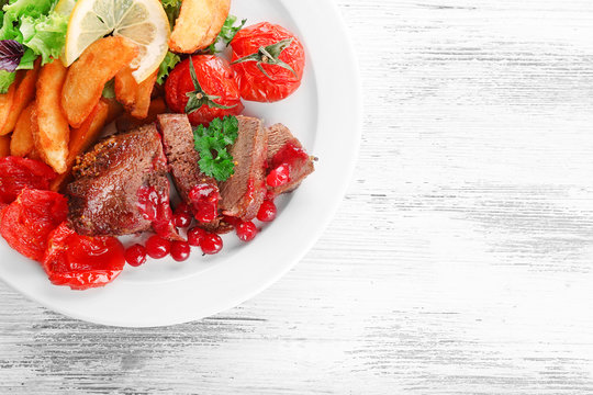 Tasty Roasted Meat With Cranberry Sauce And Roasted Vegetables On Plate, On Color Wooden Background