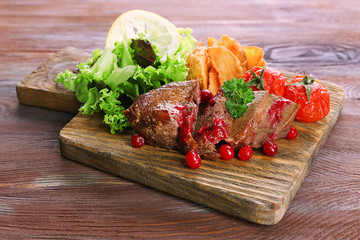 Beef with cranberry sauce, roasted potato slices on cutting board, on wooden background