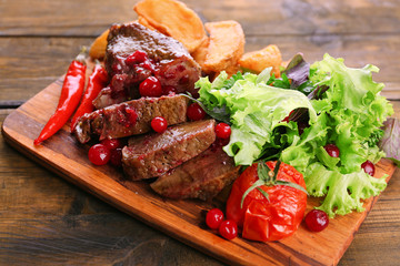 Beef with cranberry sauce, roasted potato slices on cutting board, on wooden background