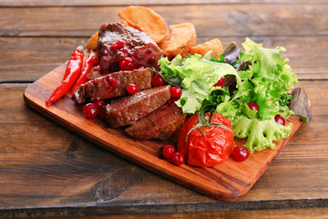 Beef with cranberry sauce, roasted potato slices on cutting board, on wooden background