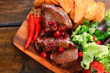Beef with cranberry sauce, roasted potato slices on cutting board, on wooden background