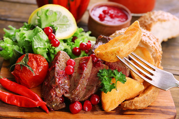 Beef with cranberry sauce, roasted potato slices on cutting board, on wooden background