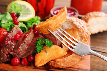 Beef with cranberry sauce, roasted potato slices on cutting board, on wooden background
