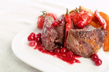 Tasty roasted meat with cranberry sauce and roasted vegetables on plate, on light background