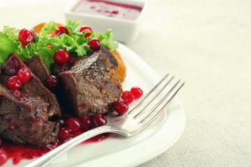 Tasty roasted meat with cranberry sauce on plate, on light background