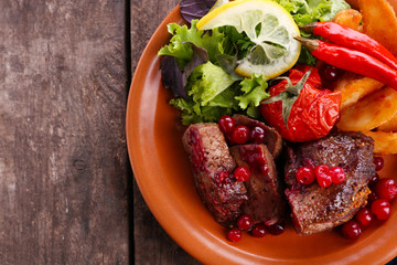 Tasty roasted meat with cranberry sauce, salad and roasted vegetables on plate, on wooden background