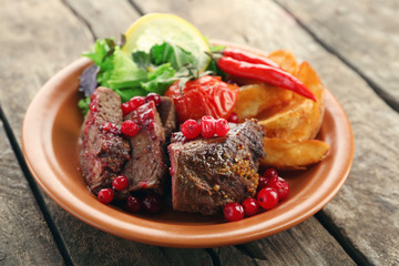 Tasty roasted meat with cranberry sauce, salad and roasted vegetables on plate, on wooden background