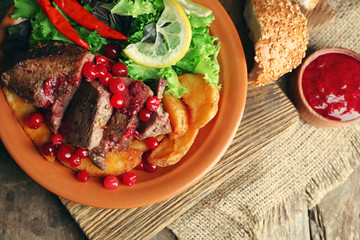 Tasty roasted meat with cranberry sauce, salad and roasted vegetables on plate, on wooden background