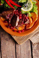 Tasty roasted meat with cranberry sauce, salad and roasted vegetables on plate, on wooden background
