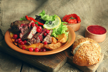 Tasty roasted meat with cranberry sauce, salad and roasted vegetables on plate, on sackcloth background