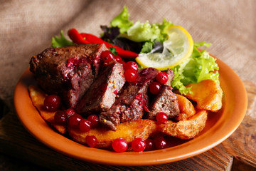 Tasty roasted meat with cranberry sauce, salad and roasted vegetables on plate, on sackcloth background